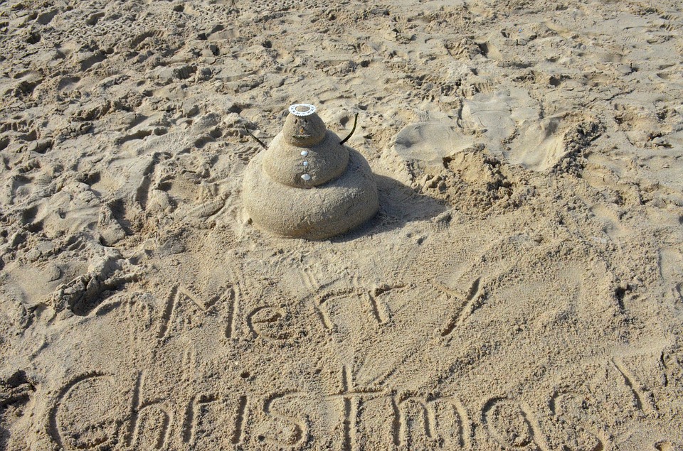 scritta merry christmas sulla spiaggia con pupazzo di sabbia